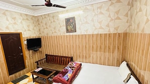 A hotel room with a bed, a wooden chair, a small table, a ceiling fan, and a television. - Hotel New Lucknow (Lucknow)