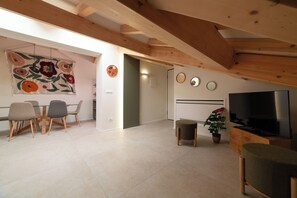 A modern living room with a dining area, wooden beams, a flat-screen TV, and a potted plant. - The Attic of My Grandparents' House (Bologna)