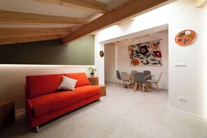 Ein modernes Wohnzimmer mit einem roten Sofa, einem Essbereich mit einem Glastisch und Stühlen sowie einer Wand mit einer Blumenweberei.