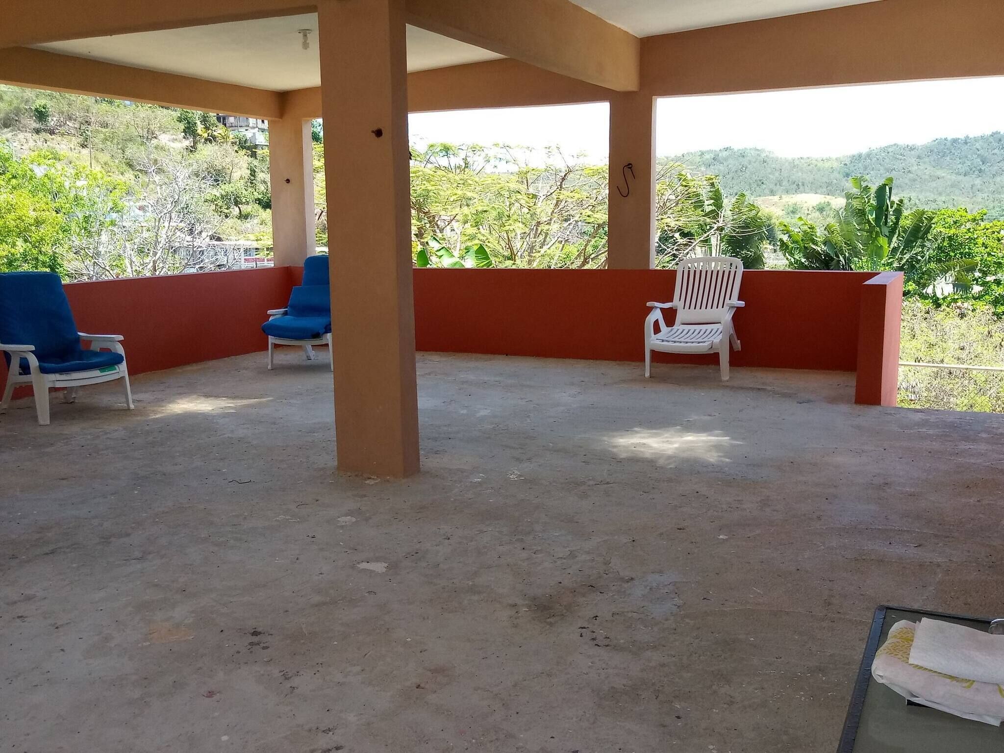 Un espacio de estar al aire libre techado con dos sillas, una azul y otra blanca, y piso de concreto.