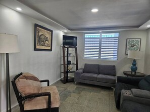 A living room with a sofa, a chair, a TV on a stand, and a window with blinds. - Spacious Beachfront Escape at Playa Guayanes for Large Groups (Yabucoa)