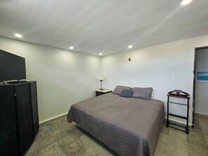 A bedroom with a bed, a desk, a chair, a TV, and a wardrobe.