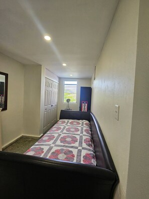 A narrow hallway with a bed at the end, a window with blinds, a door, and a wall-mounted light fixture. - Spacious Beachfront Escape at Playa Guayanes for Large Groups (Yabucoa)