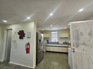A kitchen with a refrigerator, stove, and cabinets. There is a fire extinguisher on the wall.