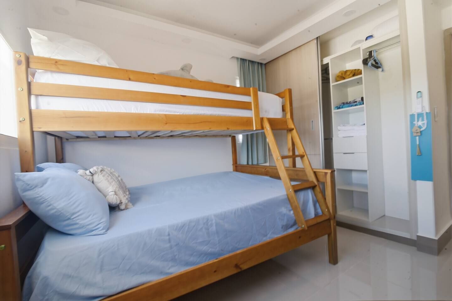 A bunk bed with a ladder, a bedside table, and a wardrobe with shelves.