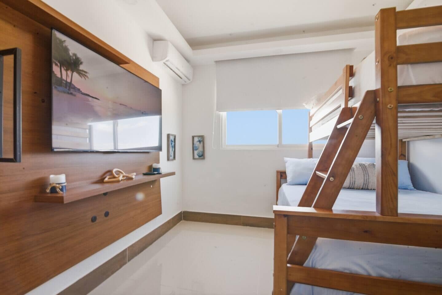 Ein Zimmer mit Etagenbett, einem an der Wand montierten Fernseher, einem kleinen Regal mit Gegenständen und einem Fenster mit Blick.