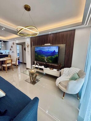 Ein modernes Wohnzimmer mit Flachbildfernseher, einer Couch, einem Essbereich und einer Küche im Hintergrund.