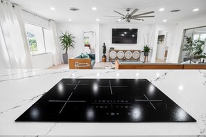 Een moderne keuken met een zwart inductiefornuis, witte marmeren aanrechtbladen en een plafondventilator.