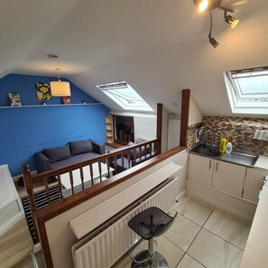 A compact living space with a kitchenette, a blue wall, a ceiling fan, and a skylight.