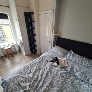A bedroom with a bed, a desk, a radiator, a door, and a shelving unit. - Private Apartment (Flat 5) (Dublin)