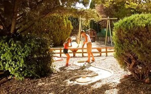 Ein Garten mit einer Holzschaukel, einem Gartenschlauch und einem Kind beim Spielen.