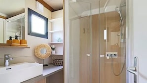 A modern bathroom with a glass shower enclosure, a sink with a mirror, and a wooden vanity.
