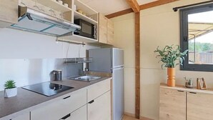 Cozinha compacta com micro-ondas embutido, geladeira e pia. Há uma pequena planta no balcão e uma janela com vista para o exterior.