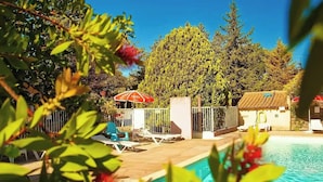 Área de piscina com espreguiçadeiras e um guarda-sol, cercada por árvores e um muro.