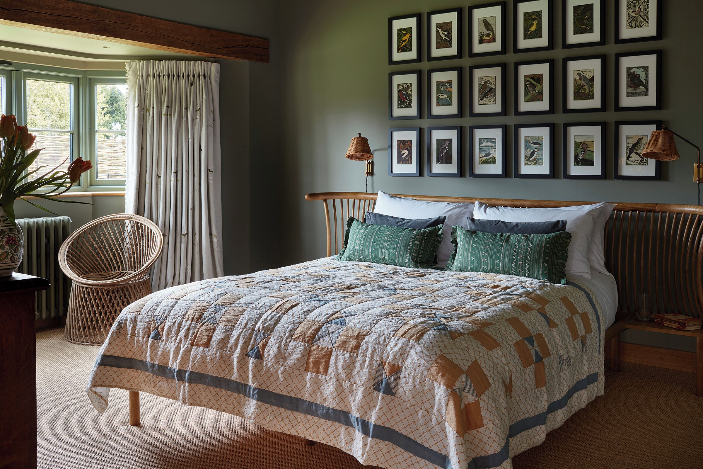 A bedroom with a bed, a chair, a wall with framed pictures, and a window with curtains.