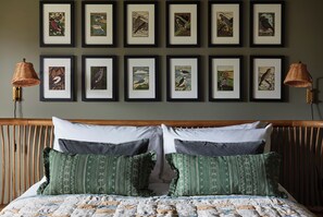 A bedroom with a bed, two wall-mounted lamps, and a series of framed bird illustrations on the wall. - Beautiful Cottage with Tennis Court and Games Barn (Hambleden)