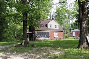 A two-story brick house with a large garage, surrounded by trees and a grassy yard.