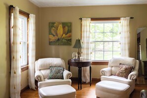 Una habitación con dos sillones blancos, una mesita con una lámpara y un cuadro en la pared.