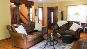 A living room with two brown leather sofas, a glass coffee table, and a patterned rug.