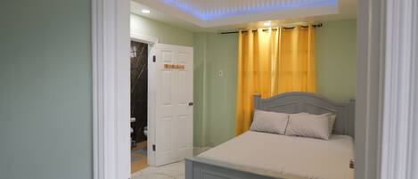 Un dormitorio con una cama, una puerta y un baño visible a través de otra puerta abierta.
