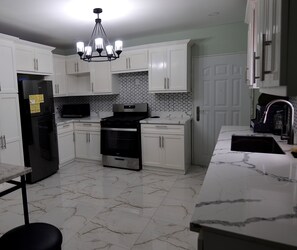 A kitchen with white cabinets, a black refrigerator, a microwave, a stove, and a chandelier. - Amazing 3-bedroom apartment with AC in charming Georgetown (Georgetown)