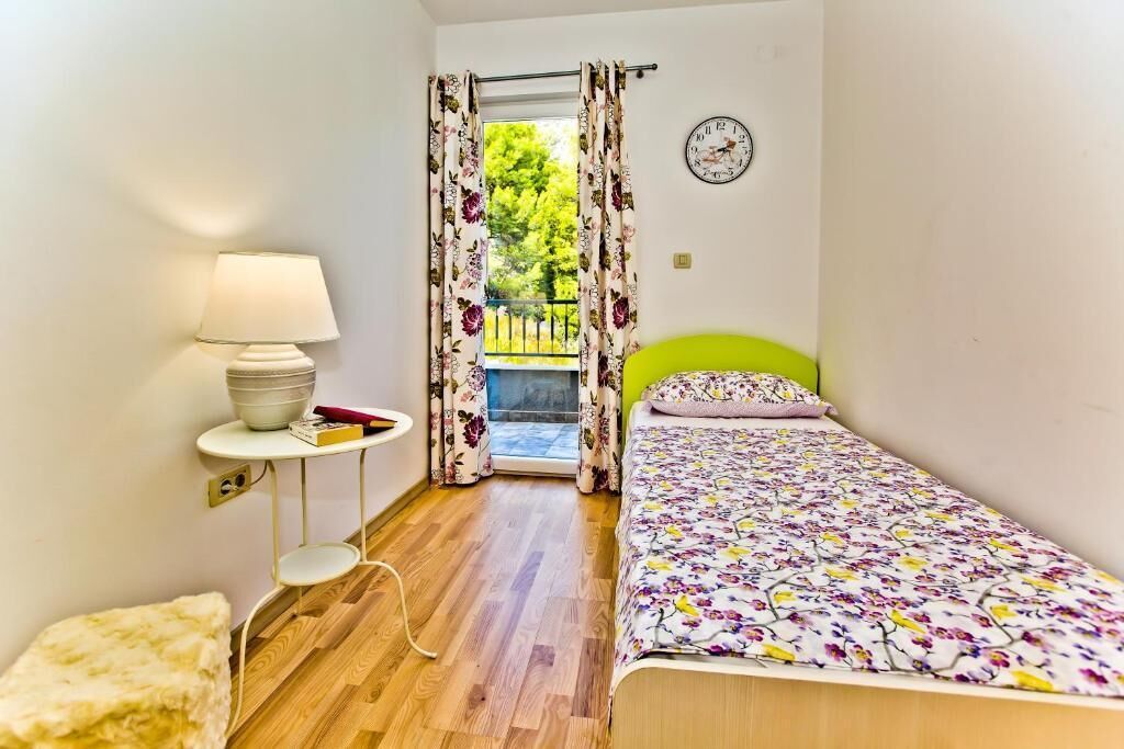 Een slaapkamer met een bed, een nachtkastje met lamp, een raam met gordijnen en een klok aan de muur.
