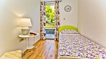 Een slaapkamer met een bed, een nachtkastje met lamp, een raam met gordijnen en een klok aan de muur.