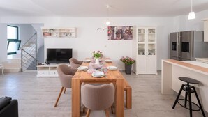 Een moderne woonkamer met een eettafel, stoelen, een televisie en een keuken met een koelkast en kasten.