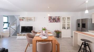 Een moderne woonkamer met een eettafel, stoelen, een televisie en een keuken met een koelkast en kasten.