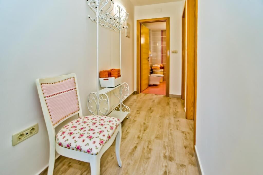 Un couloir avec une chaise blanche à motifs floraux, une étagère métallique blanche et un lustre.