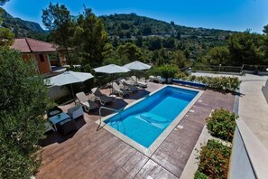 A swimming pool with lounge chairs and umbrellas, surrounded by greenery and a mountainous backdrop. - Spacious 5-bedroom apartment in marvelous Milna Hvar with AC (Milna Hvar)