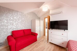 Une pièce avec un canapé rouge, une commode blanche, un téléviseur à écran plat et un mur orné d’un motif.