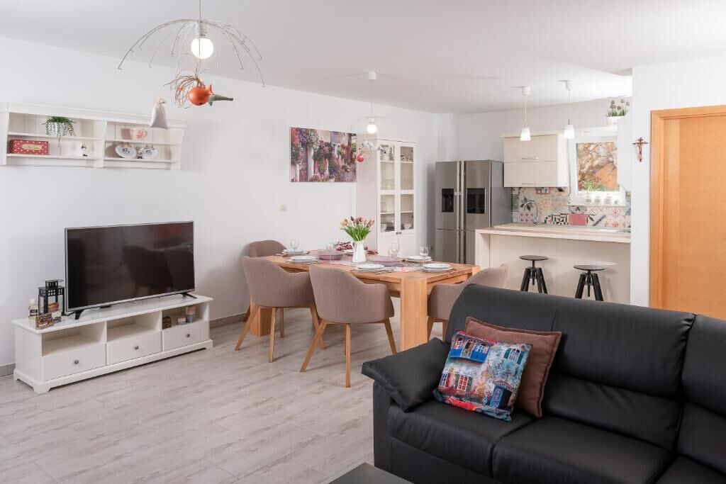 Un salon moderne avec un canapé noir, un téléviseur et un coin repas comprenant une table et des chaises en bois.