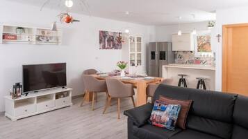 Un salon moderne avec un canapé noir, un téléviseur et un coin repas comprenant une table et des chaises en bois.