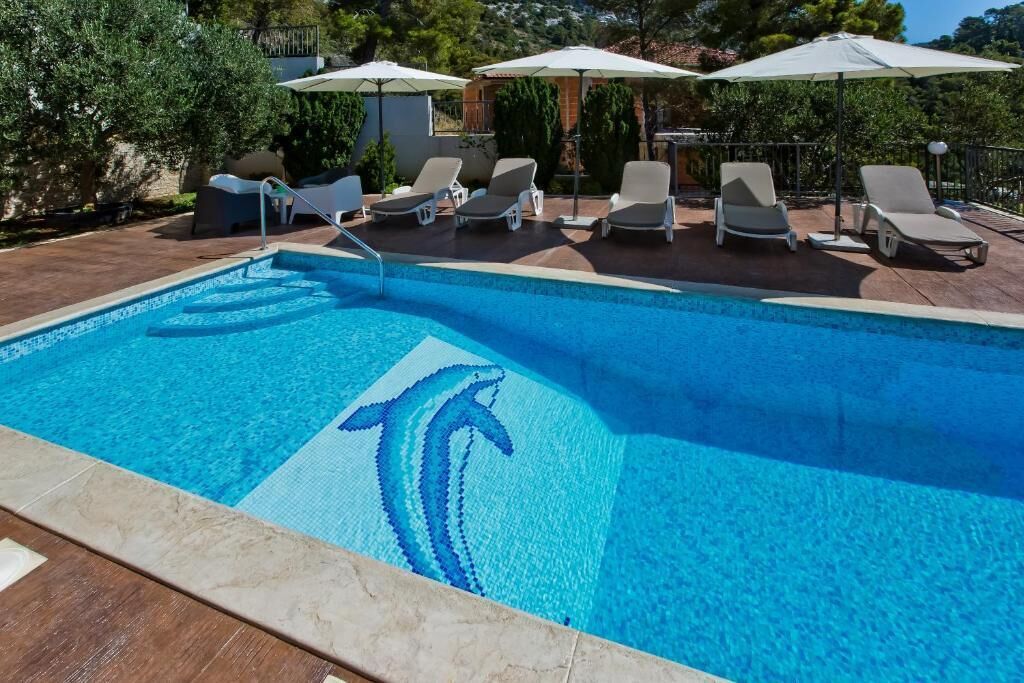 Une piscine ornée d’une mosaïque représentant un dauphin, entourée de chaises longues et de parasols.