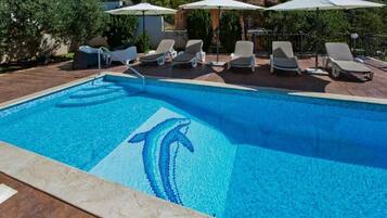 Une piscine ornée d’une mosaïque représentant un dauphin, entourée de chaises longues et de parasols.