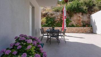 Une terrasse extérieure avec une table et des chaises, un pot de fleurs et un drapeau.