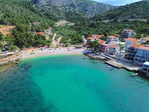 A coastal town with a clear turquoise bay, buildings with red roofs, and a rocky hillside in the background. - Spacious 5-bedroom apartment in marvelous Milna Hvar with AC (Milna Hvar)