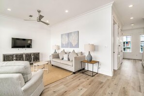 A modern living room with a sofa, a coffee table, a TV, and artwork on the wall. - Beachfront Bliss Beach House (Orange Beach)