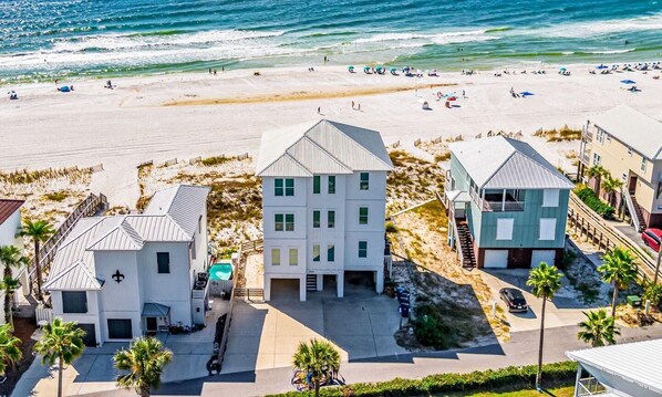 A beachfront property with multiple buildings, including a two-story house with a front porch and a garage. - Beachfront Bliss Beach House (Orange Beach)