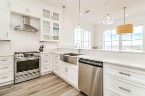 A modern kitchen with white cabinetry, stainless steel appliances, and pendant lighting. - Beachfront Bliss Beach House (Orange Beach)