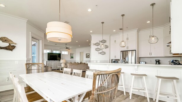 A modern kitchen with white cabinetry, a central island with bar stools, and pendant lighting. - Beachfront Bliss Beach House (Orange Beach)