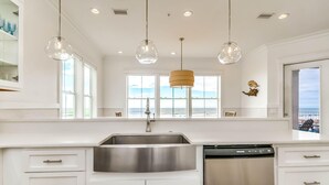 A modern kitchen with a stainless steel sink, white cabinets, and pendant lights. - Beachfront Bliss Beach House (Orange Beach)