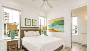 A bedroom with a large bed, a ceiling fan, a window with a view, and a painting on the wall. - Beachfront Bliss Beach House (Orange Beach)