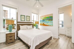 A bedroom with a large bed, a ceiling fan, a window with a view, and a painting on the wall. - Beachfront Bliss Beach House (Orange Beach)