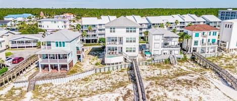 A coastal residential area with beachfront properties featuring balconies, some with pool access, and a wooden boardwalk leading to the beach.