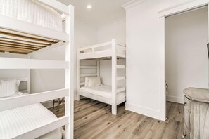 A room with bunk beds, a wooden floor, and a white door. - Beachfront Bliss Beach House (Orange Beach)