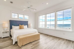 A bedroom with a large bed, a ceiling fan, and a view of the ocean. - Beachfront Bliss Beach House (Orange Beach)