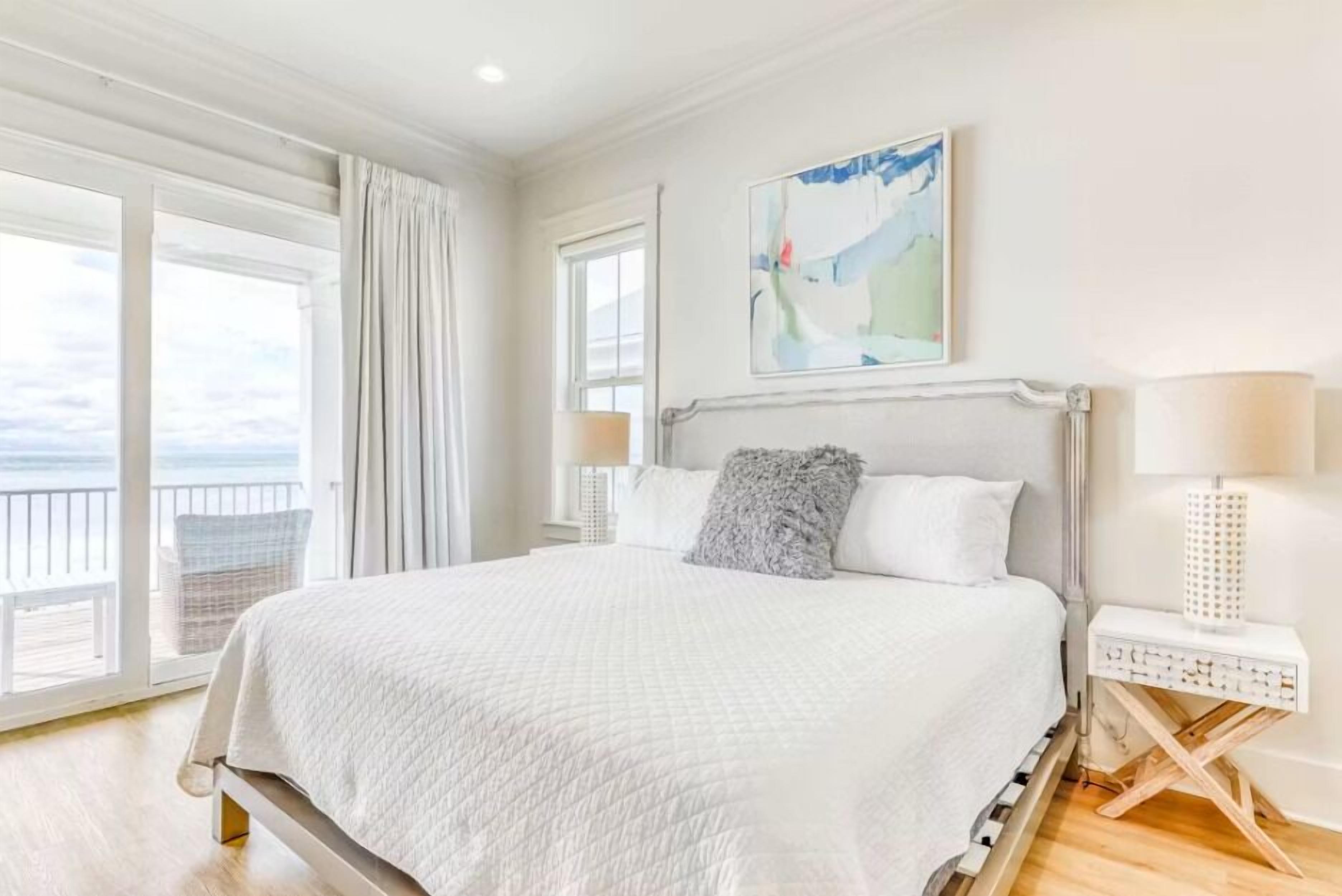 A hotel room with a large bed, a view of the sea, and a painting on the wall.