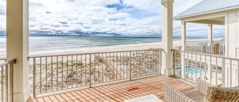 Un espacio al aire libre techado con vistas a la playa y al océano, que incluye una piscina y mobiliario exterior.